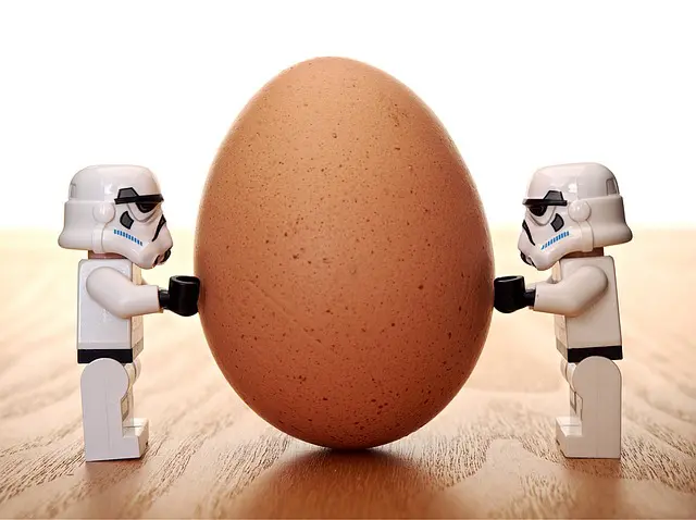 Two storm trooper lego figures holding an egg on a wooden table