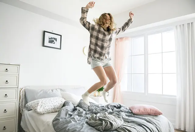 a woman in a plaid shirt is jumping on a bed