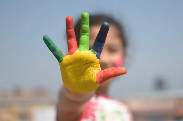 an individual reaching their hand out and their hand is painted yellow, green, red, and blue