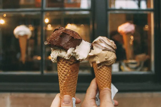 two hands holding up two ice cream cones in front of windows