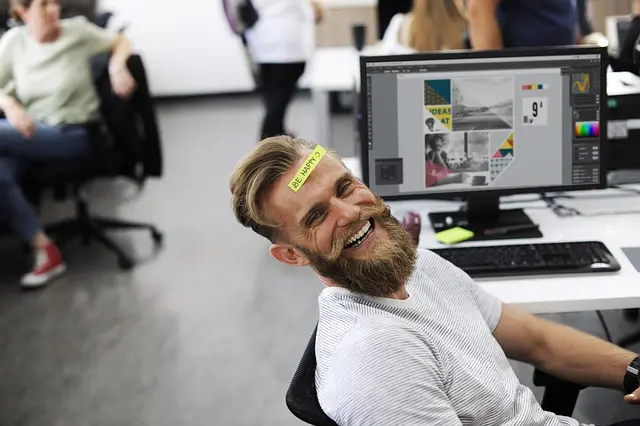 a man with a sticker on his head that says "hey happy'' is sitting in front of a computer