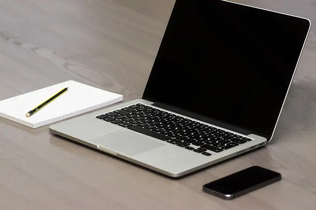 a phone, laptop, and notebook and paper sitting on a wooden surface