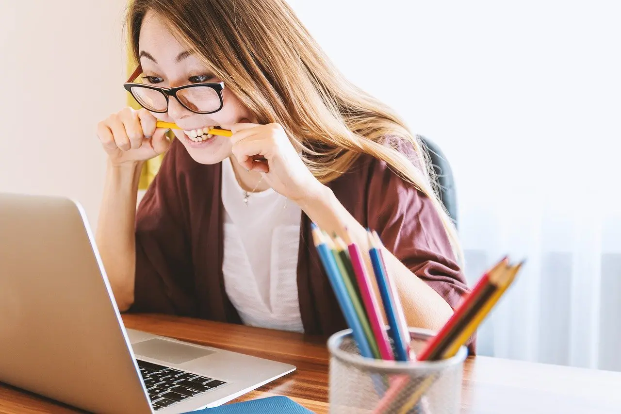 a woman biting a pencil in front of a laptop