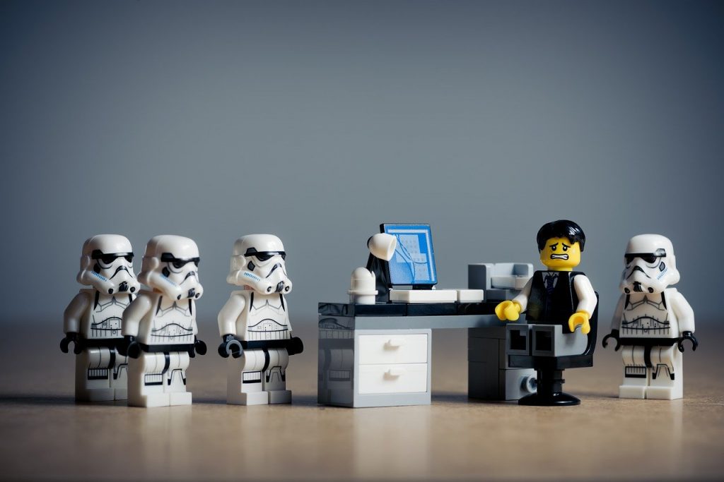 4 lego stormtroopers are approaching an individual at their desk with a nervous look on their face