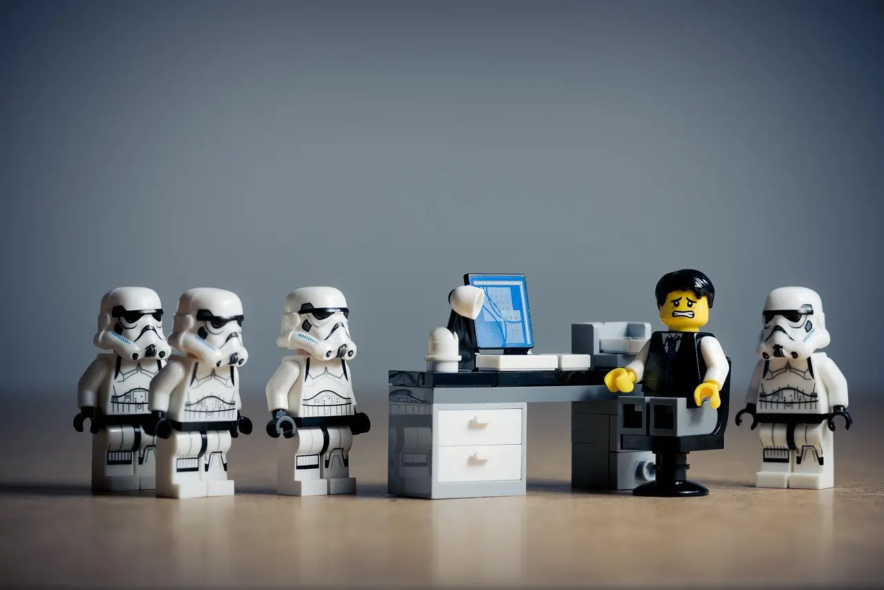4 lego stormtroopers are approaching an individual at their desk with a nervous look on their face