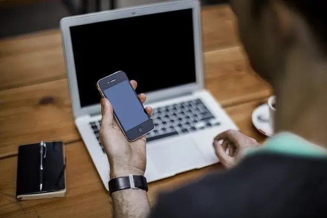 a man is holding a cell phone in front of a laptop computer .