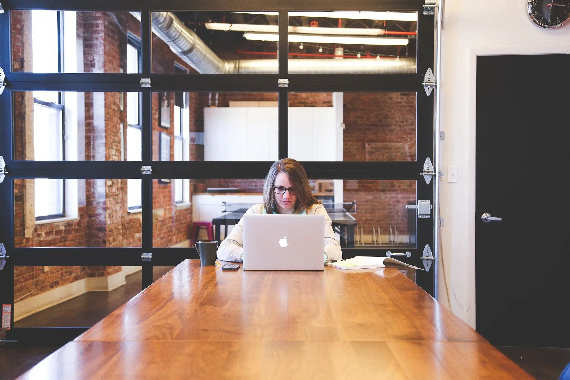 a woman sits at a table using an apple laptop
