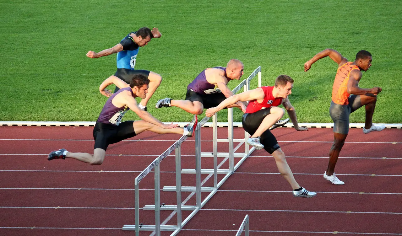 five runners jumping over hurdles on a track