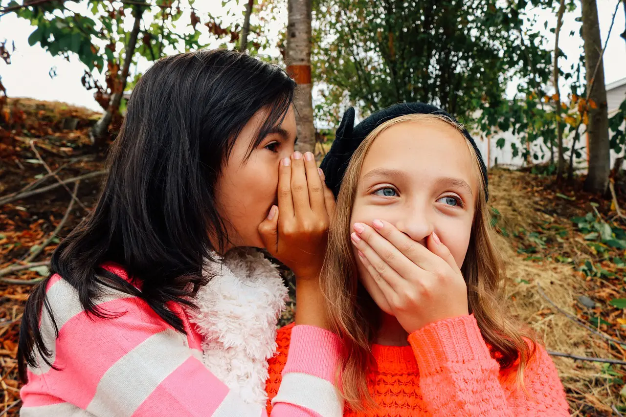 a girl whispering a secret into another girl 's ear