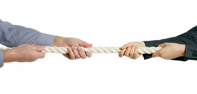 two pairs of hands on different sides of a rope each pulling the rope towards their side