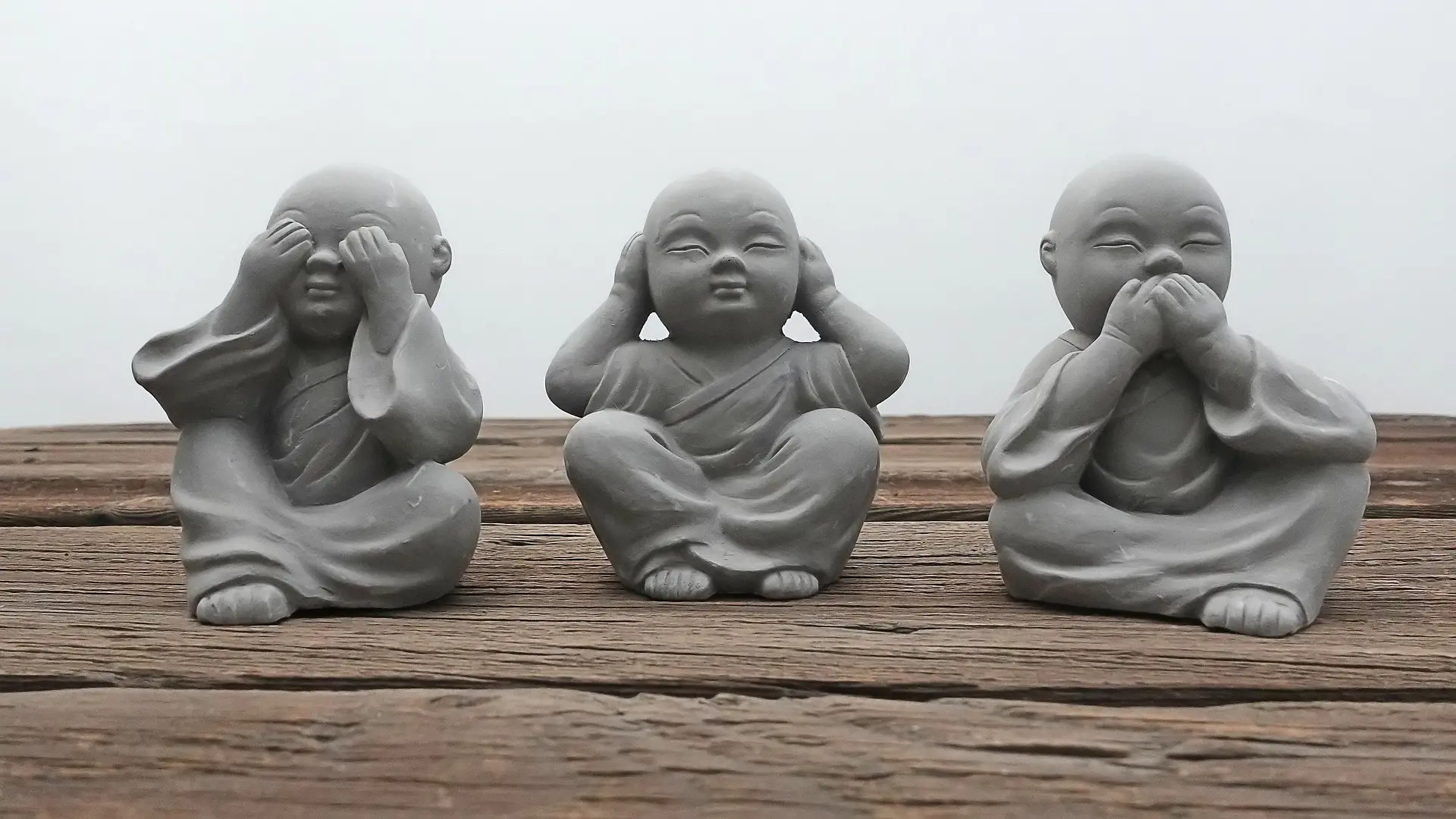 three statues sit on a wooden table covering their eyes ears and mouths