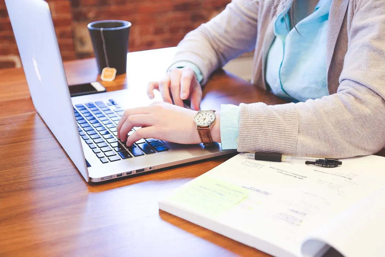 a woman wearing a watch is typing on a laptop