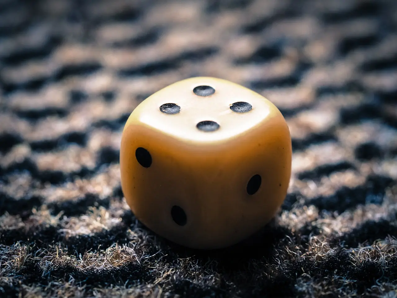 Closeup of yellow dice with four black dots on the top