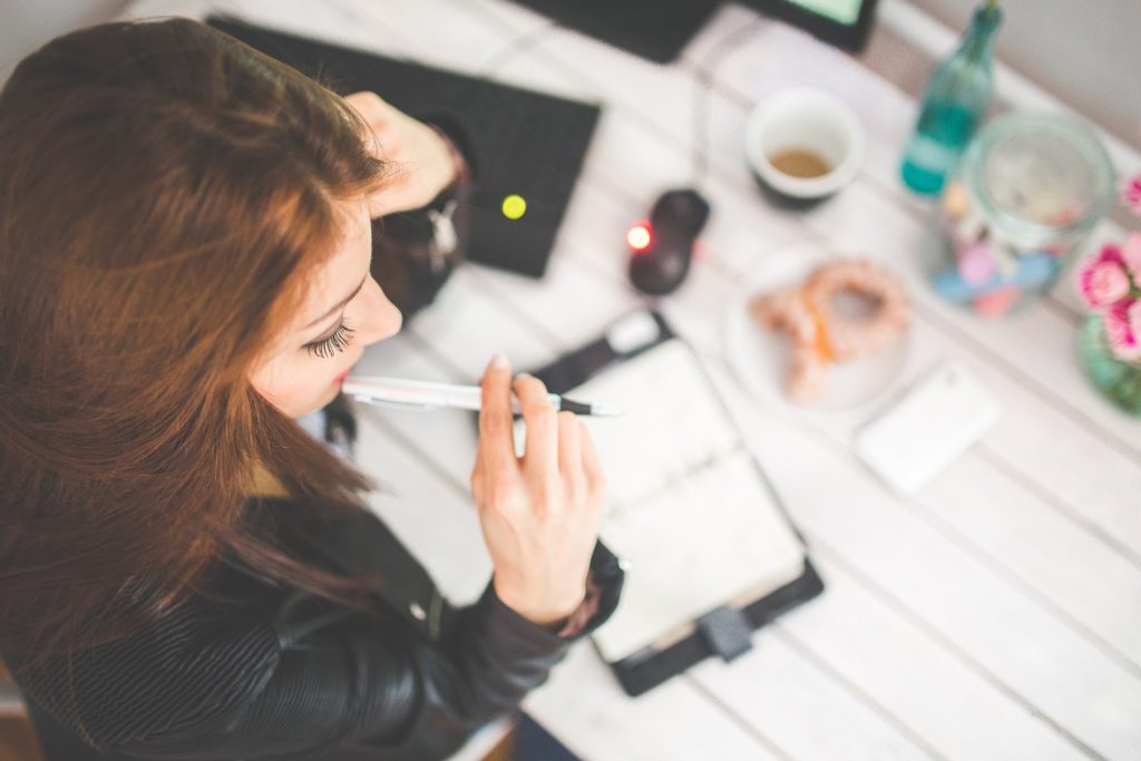 a woman sitting at a desk with a pen in her mouth