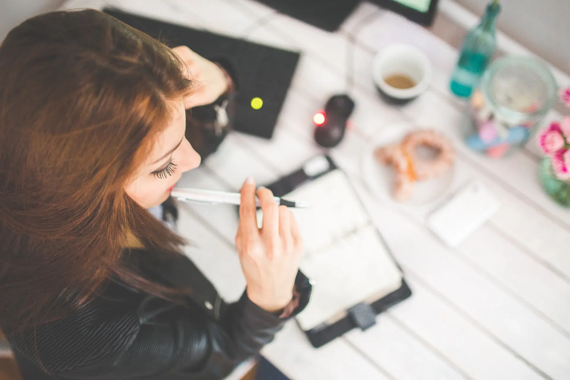 a woman sitting at a desk with a pen in her mouth