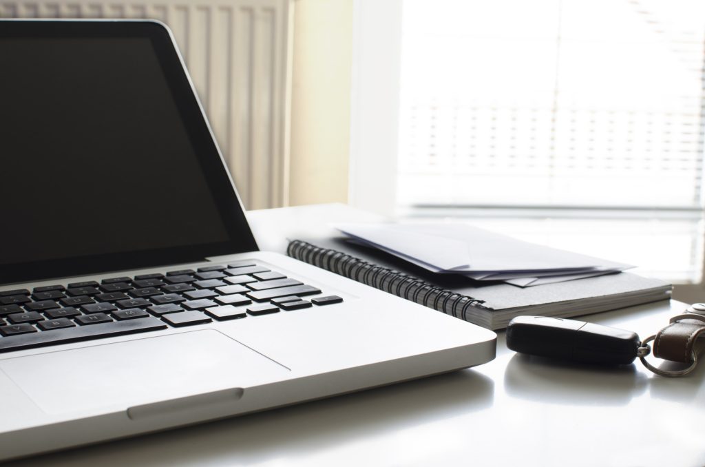 a laptop sits on a desk next to a notebook and a car key