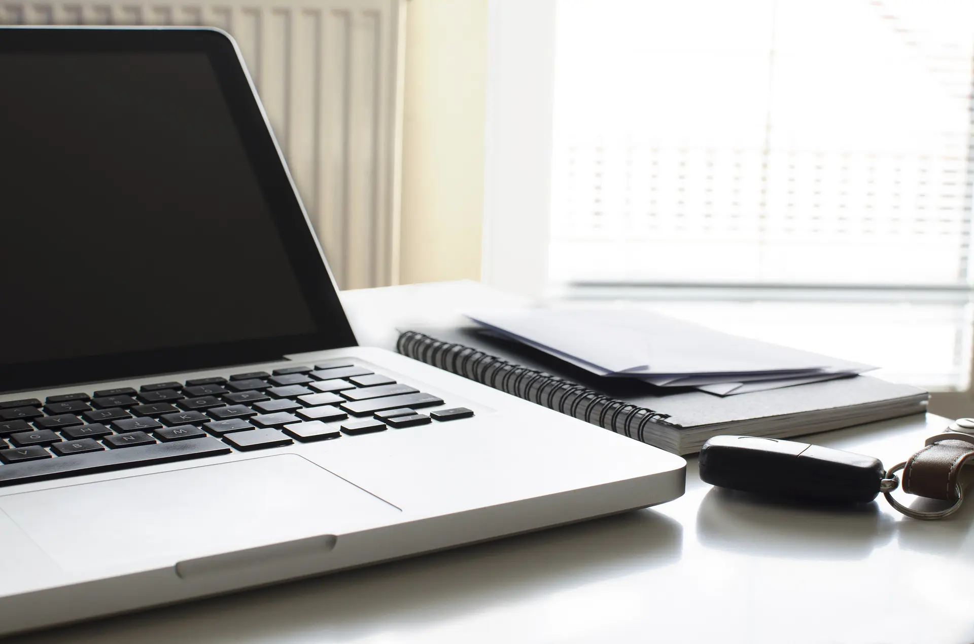 a laptop sits on a desk next to a notebook and a car key