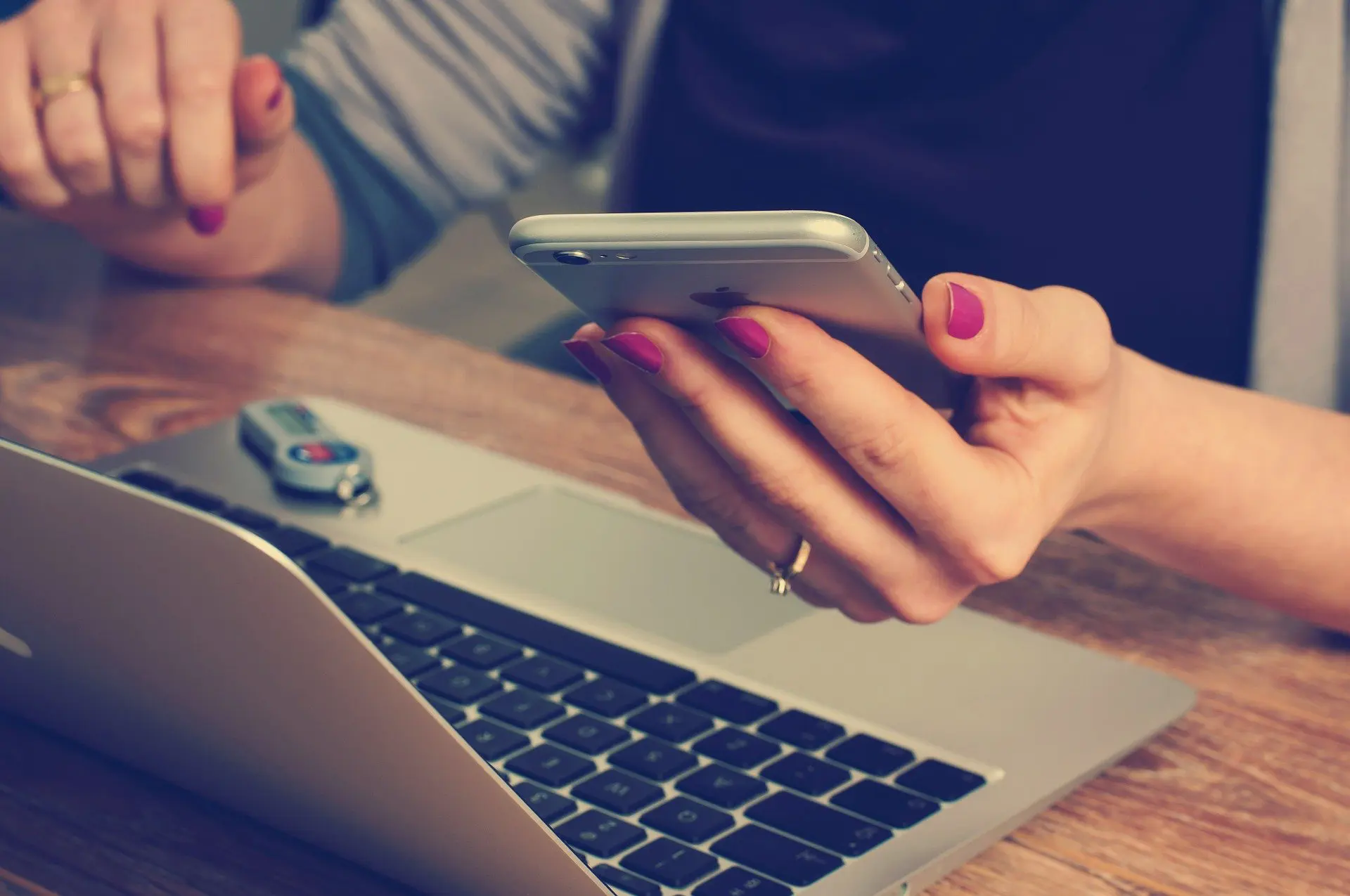 a hand holding a phone with a computer in the background