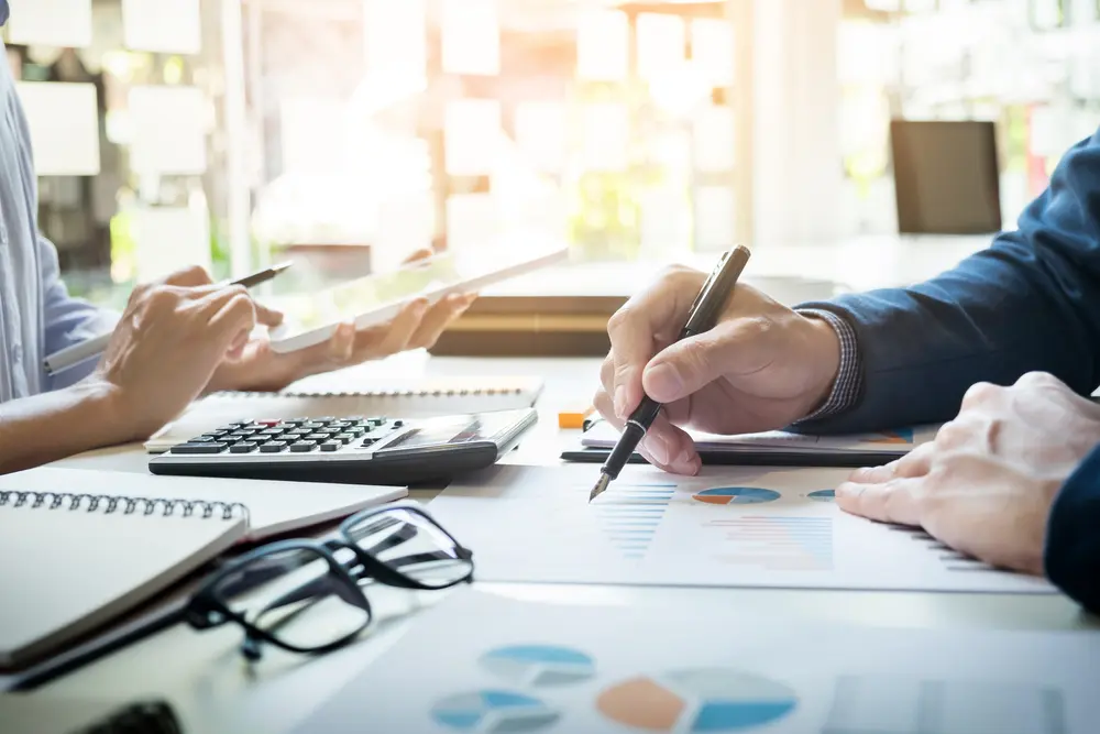 Business man writing on a piece of paper while another man looks at a tablet