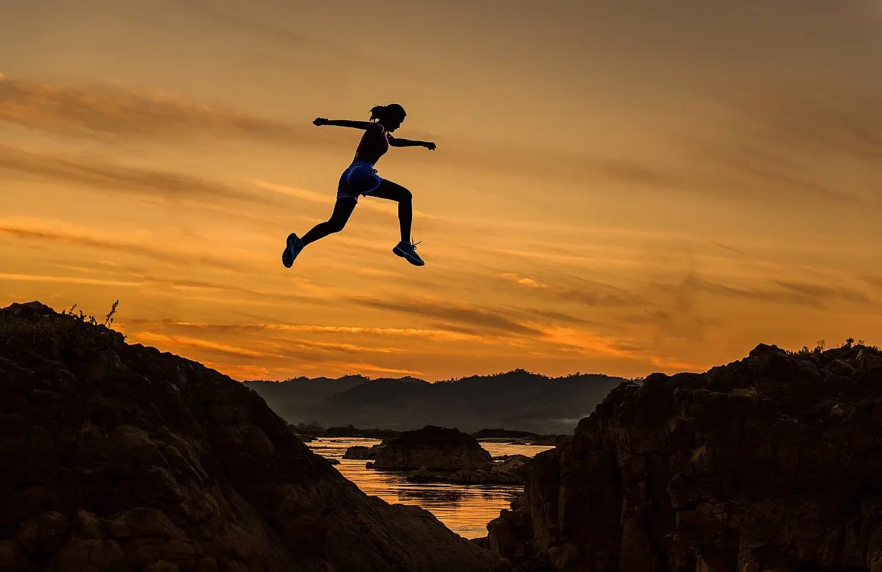 silhouette of a woman jumping over a river