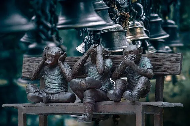 three statues of monkeys sitting on a bench covering their ears and mouths .