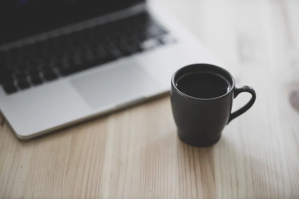a cup of coffee sitting on a wooden table in front of a laptop