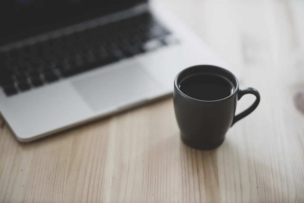 a cup of coffee sitting on a wooden table in front of a laptop