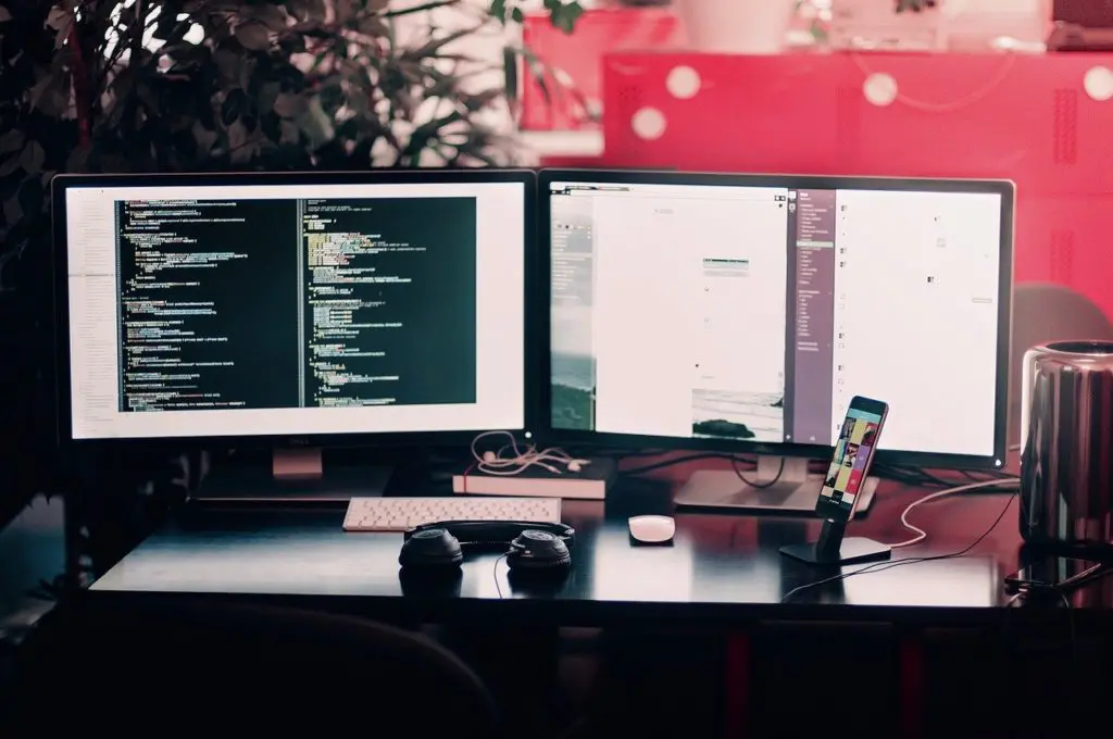 two computer monitors on a desk with one that says ' slack ' on it