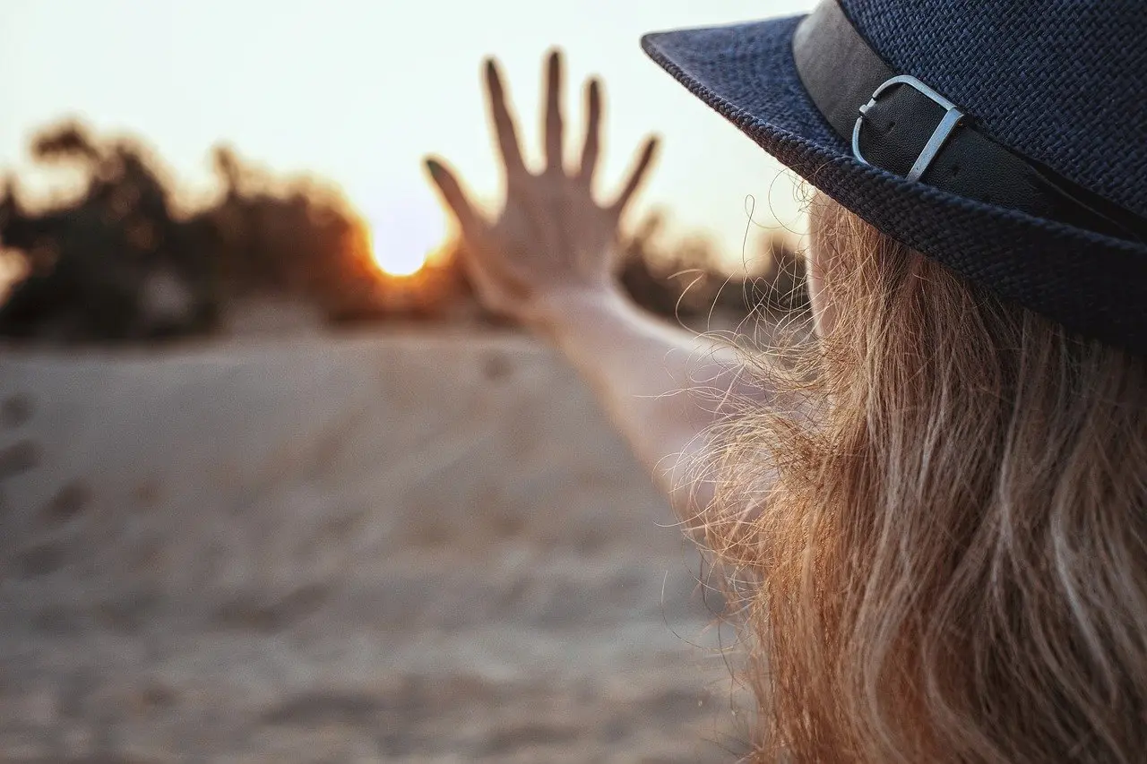 a view from behind a woman's face with her arm extended out towards a sunset