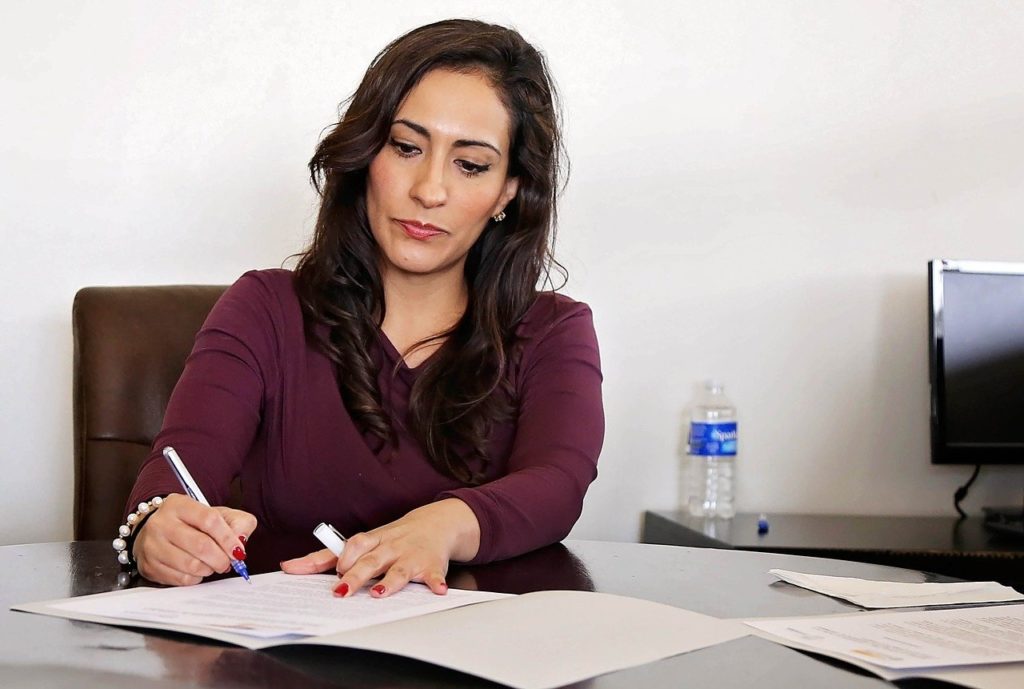 a woman sits at a desk writing on a piece of paper