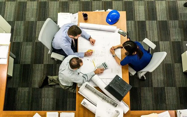 a group of people are sitting around a table looking at blueprints