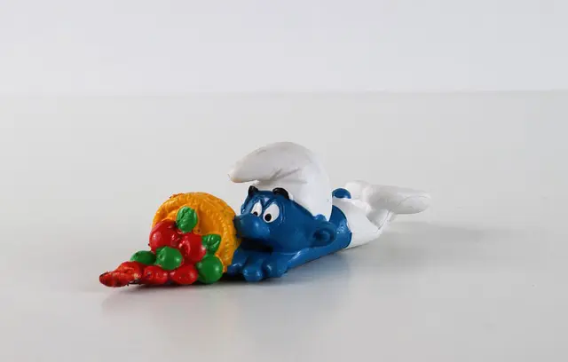 a smurf laying down spilling his basket of red and green items