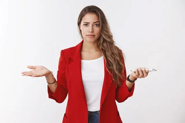 a woman in a red jacket is shrugging her shoulders while holding a cell phone