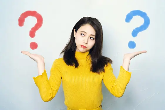 a woman in a yellow sweater is holding two question marks in her hands .