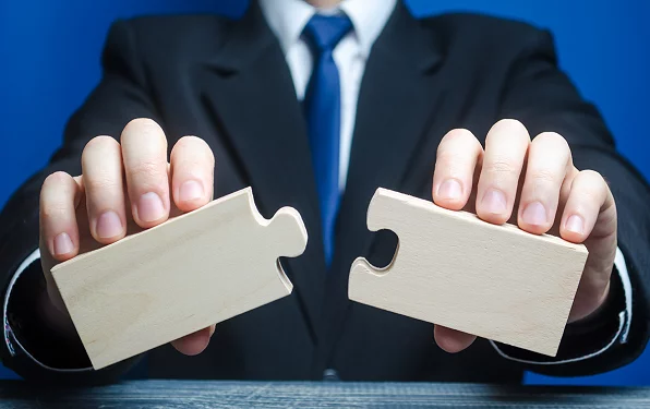 Man in a suit and tie is holding two wooden puzzle pieces