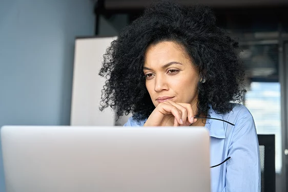 a woman with glasses in her hand looking pensively at a computer screen