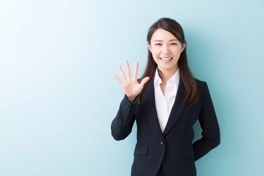 a woman in a suit and white shirt holds up five fingers