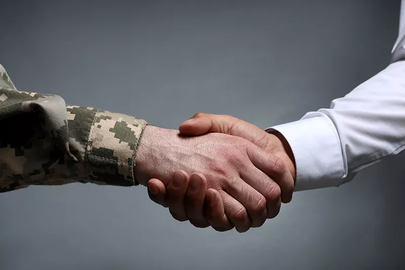 a man in a military uniform shakes hands with a man in a white shirt