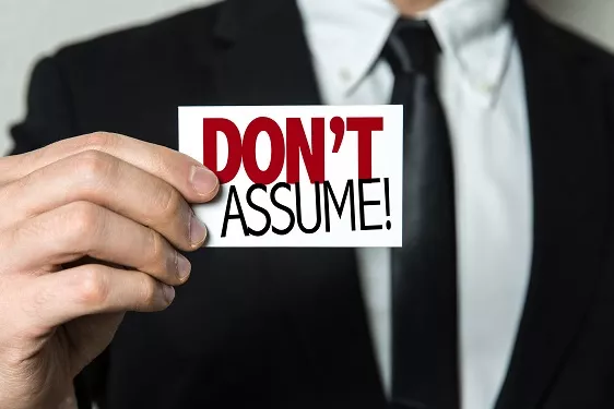 a man in a suit and tie is holding a card that says don't assume